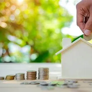 Hand putting coins in a piggy back that looks like a house