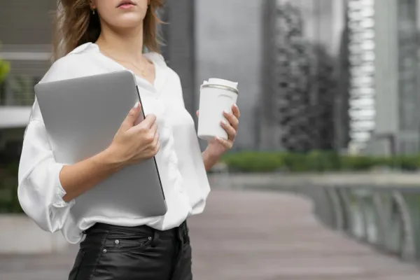 Woman CEO holding a laptop and coffee walking outside.