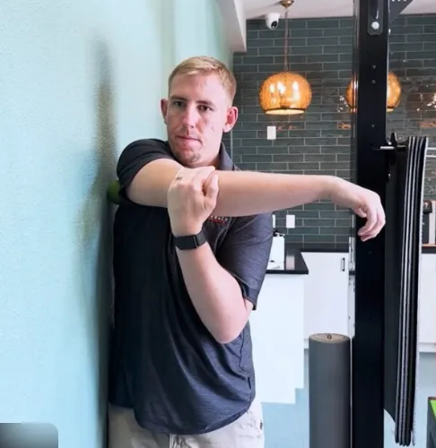 Man reaching overhead in a kitchen while gripping his shoulder in pain, showing difficulty lifting the arm due to shoulder injury