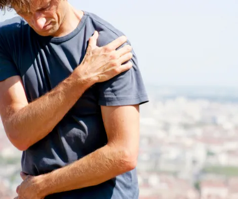 Adult sitting at home holding their shoulder in frustration after recurring shoulder pain despite previous treatment