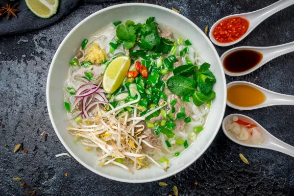 Eine dampfende Schale Pho Bo mit frischen Kräutern und Gewürzen, symbolisch für die vietnamesische Küche und Kultur.