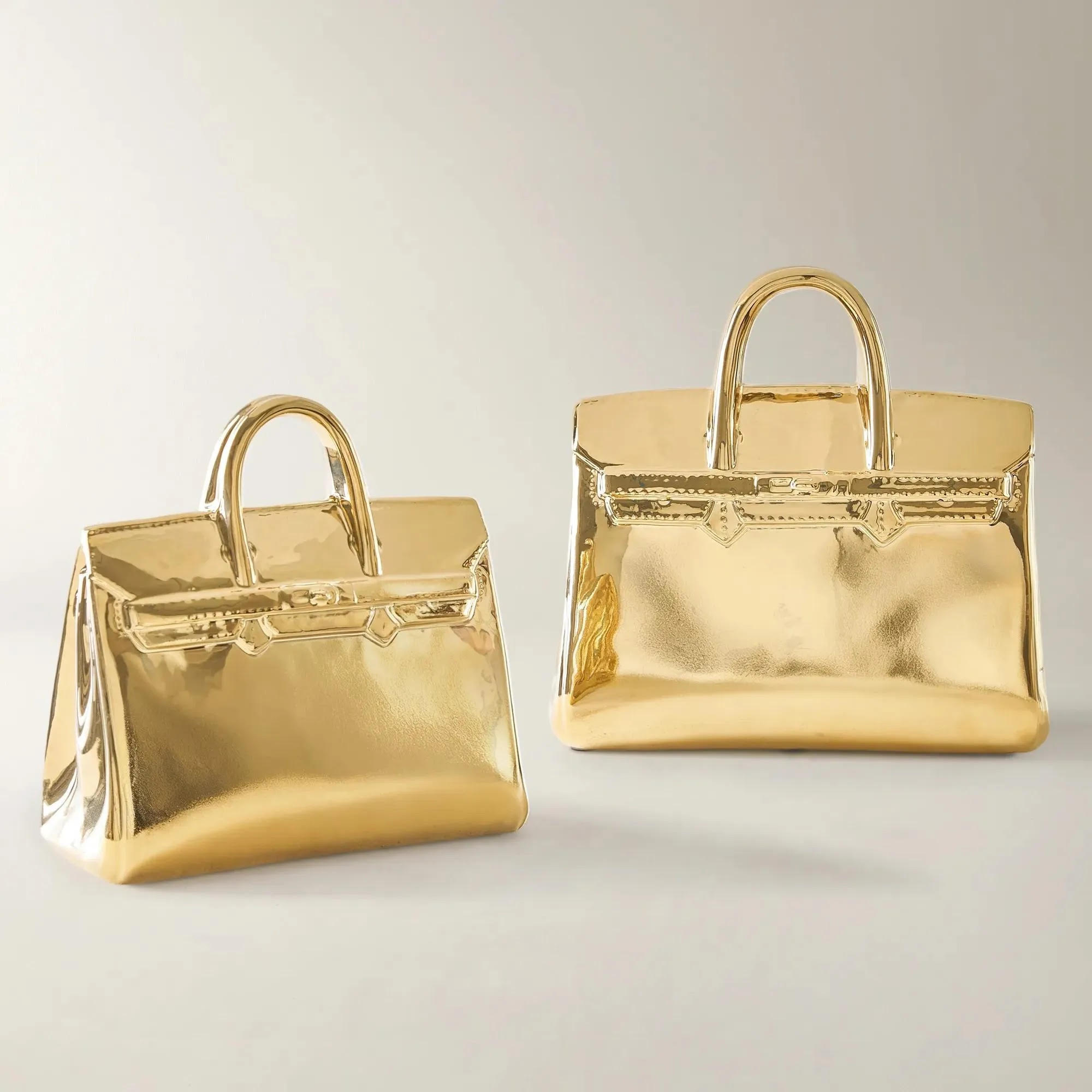 Gold metallic handbag sculpture on white background, luxury fashion accessory with reflective gold finish and structured top handle design.