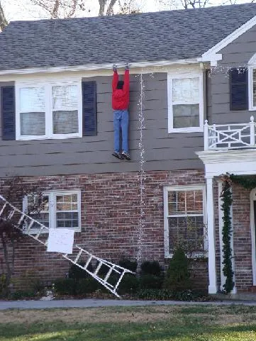 Person about to fall while hanging Christmas lights on a house, highlighting the need for safety precautions.