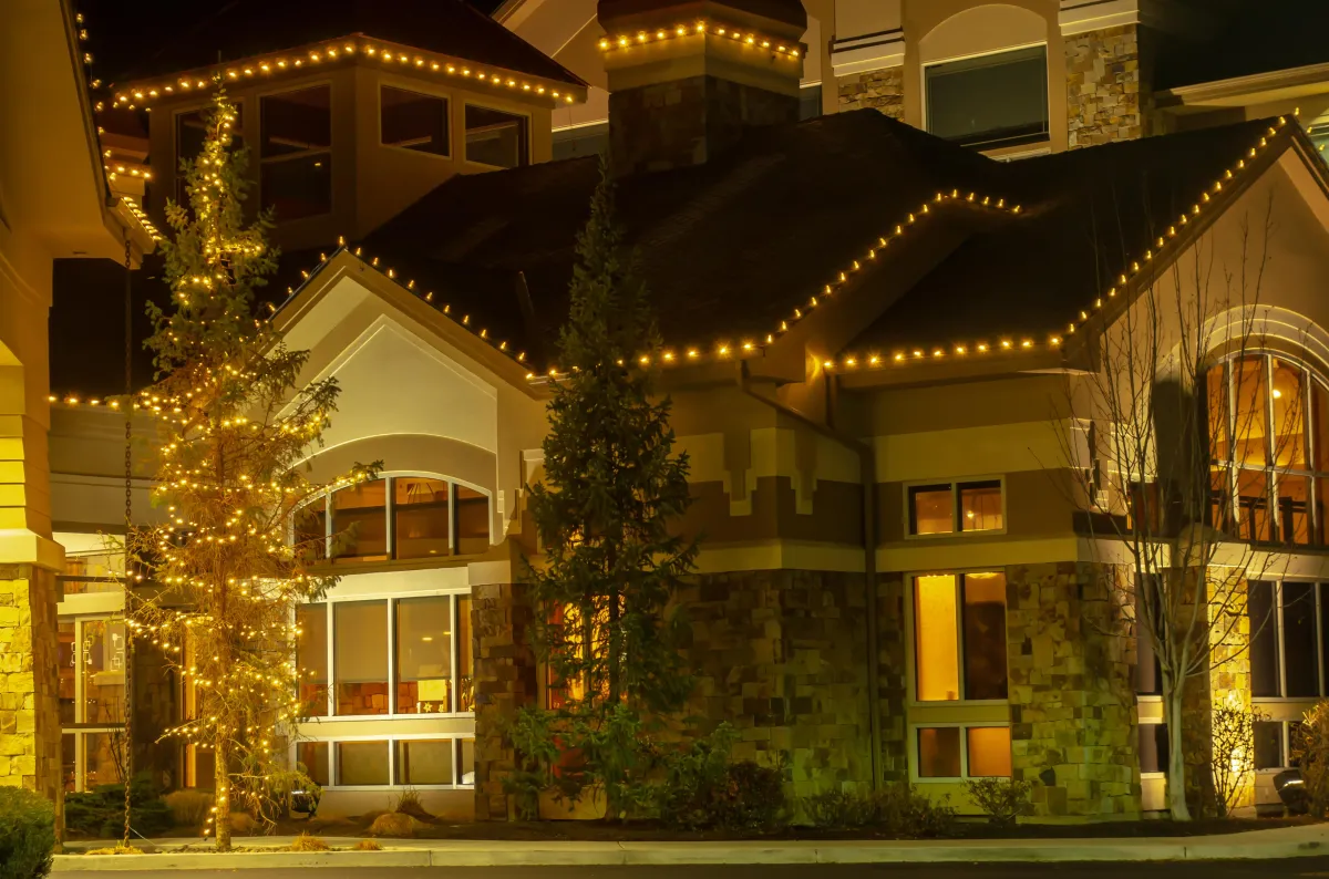 A beautifully decorated home with various types of Christmas lights illuminating the roofline, windows, and yard, creating a festive holiday atmosphere.