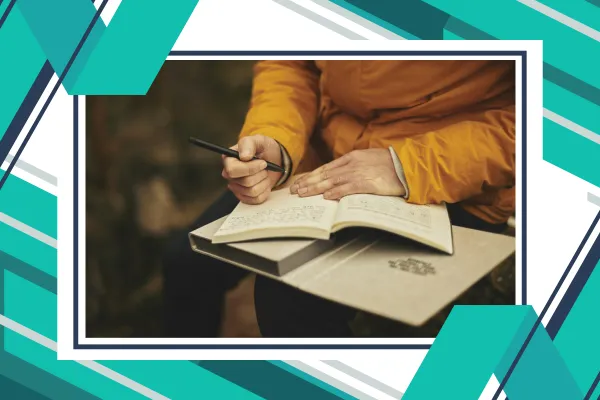 Woman in a yellow jacket sitting outside journalling.