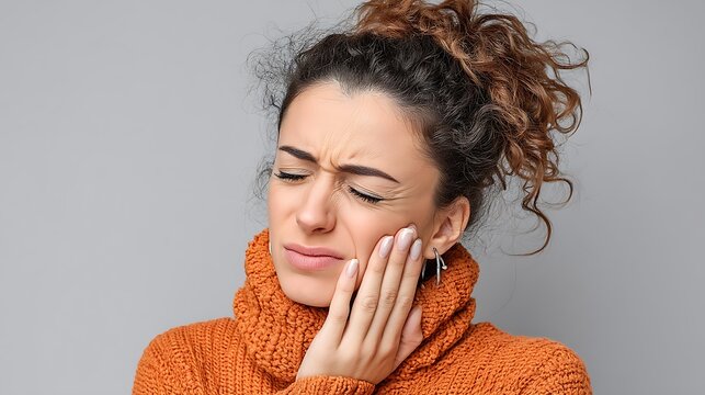 Woman touching her jaw to indicate tension or discomfort related to TMJ pain.