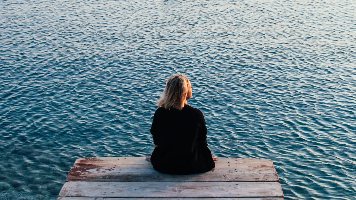 A person sitting alone at sunrise, eyes closed, hand over heart.