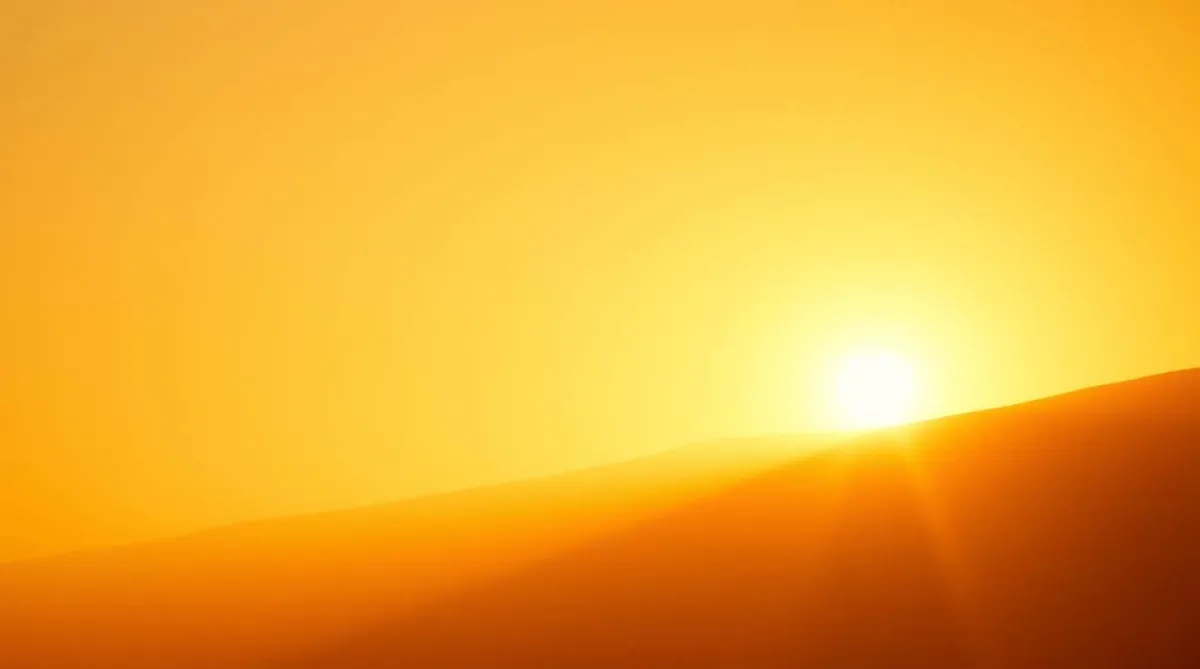 Warm golden sun setting behind mountain silhouette in amber sky