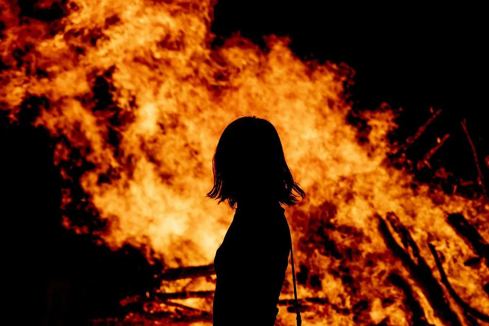 A woman stands strong in front of a burning house, symbolizing resilience. Get Christian counseling in 60637 to start healing today.