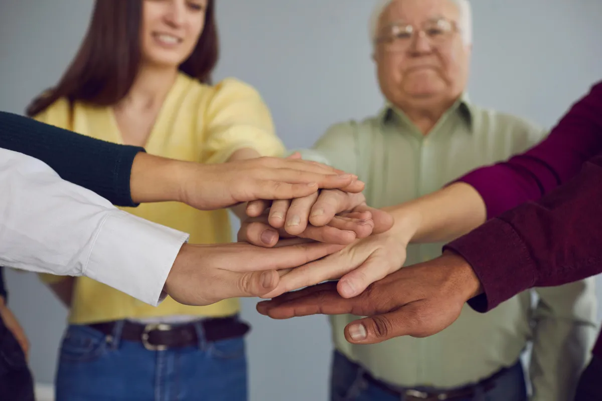 A diverse group of people standing together with their hands stacked in a team gesture, symbolizing unity, teamwork, and collaboration.