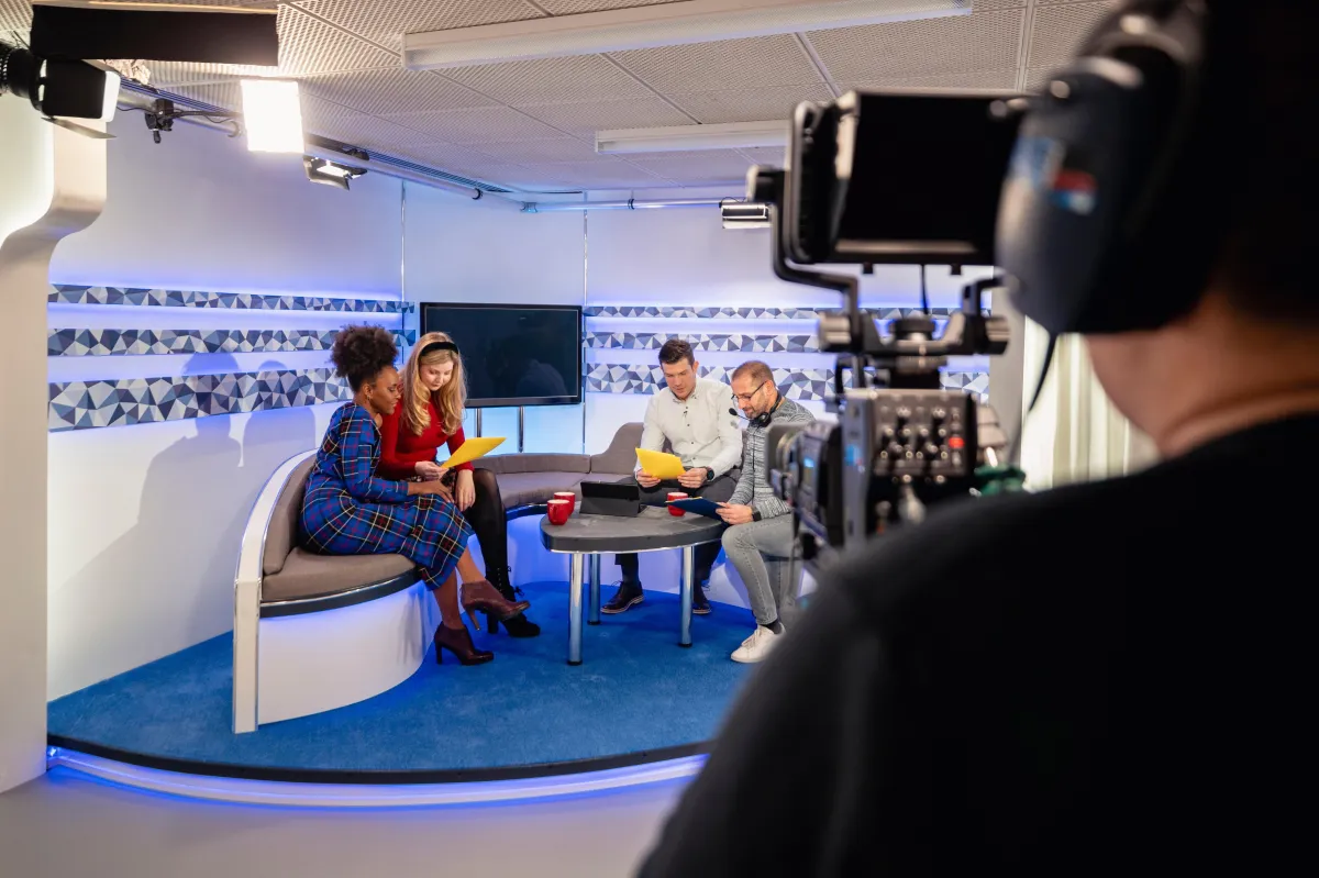 Behind-the-scenes view of a diverse group of professionals preparing for a video shoot in a modern studio, with a camera operator in the foreground.