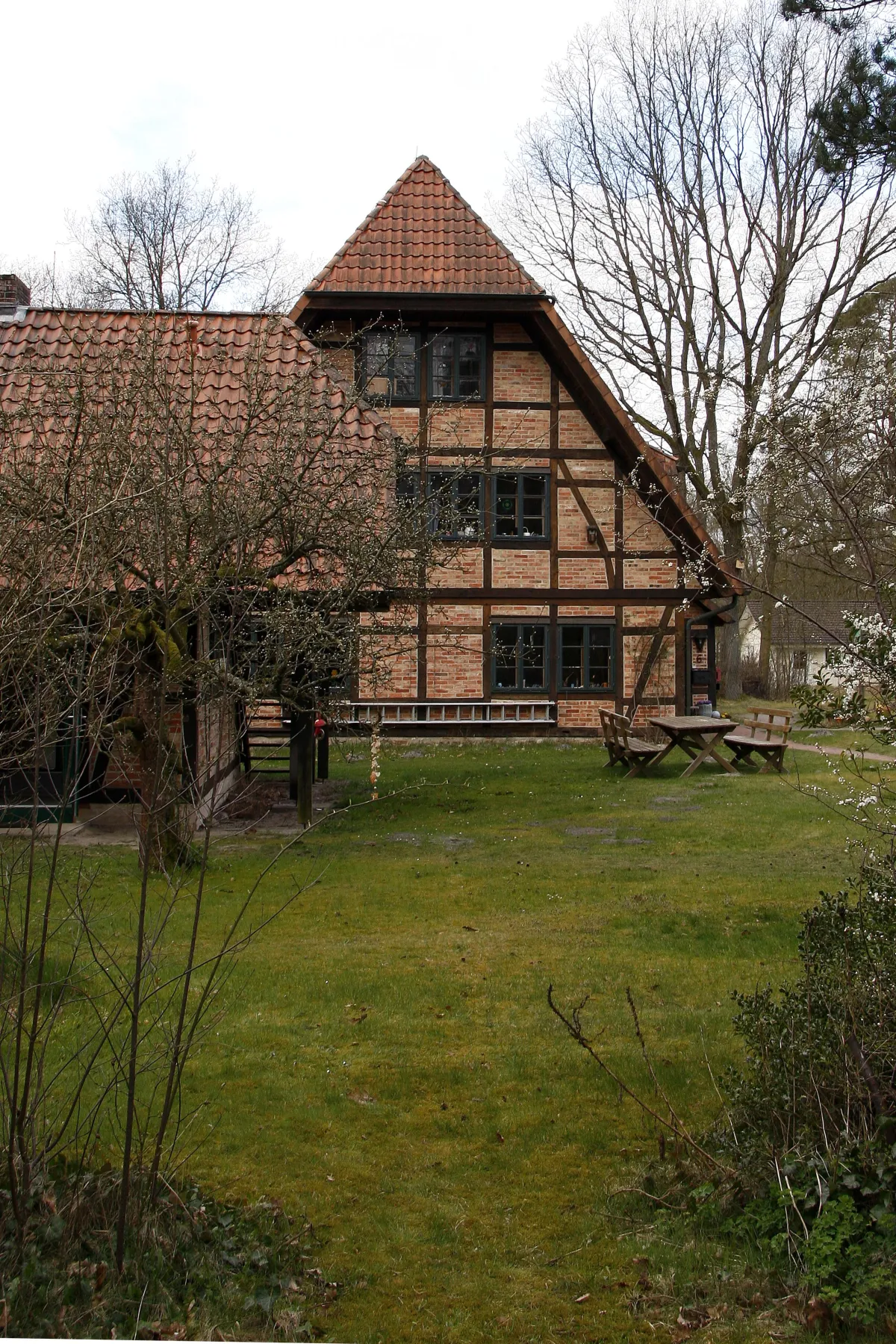 Nahansicht einer Fachwerkfassade mit großen Fenstern; davor Wiese und Sitzbank.