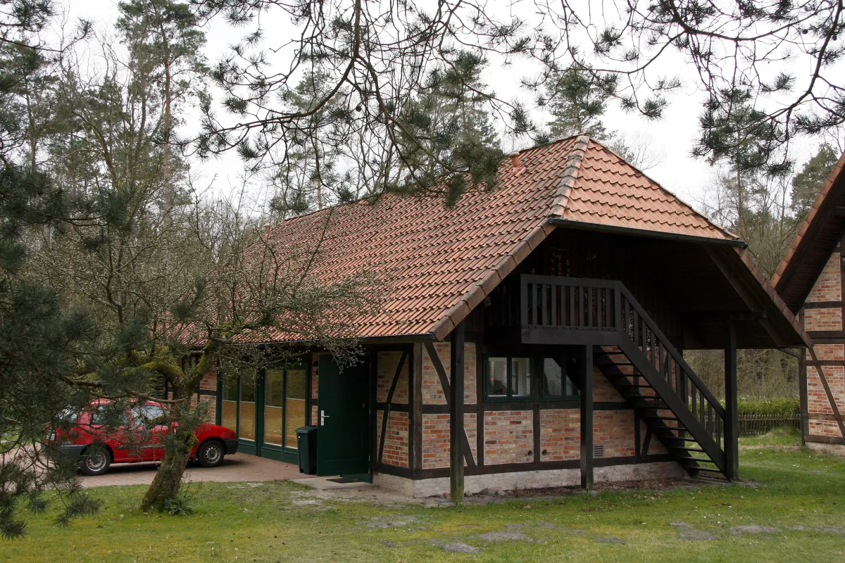 Fachwerkhaus mit Außentreppe in grüner Hofanlage; seitliche Ansicht mit Bäumen und Wiese.