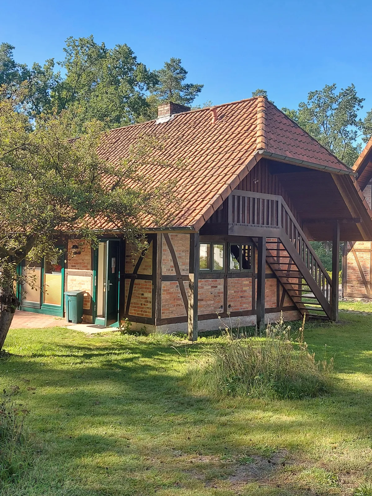 Kleines Fachwerkgebäude mit rotem Ziegeldach und außenliegender Holztreppe zum Obergeschoss.