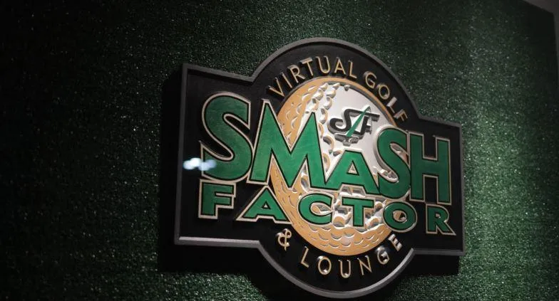 Logo of an indoor golf facility featuring golf clubs and a golf ball against a backdrop of green grass.