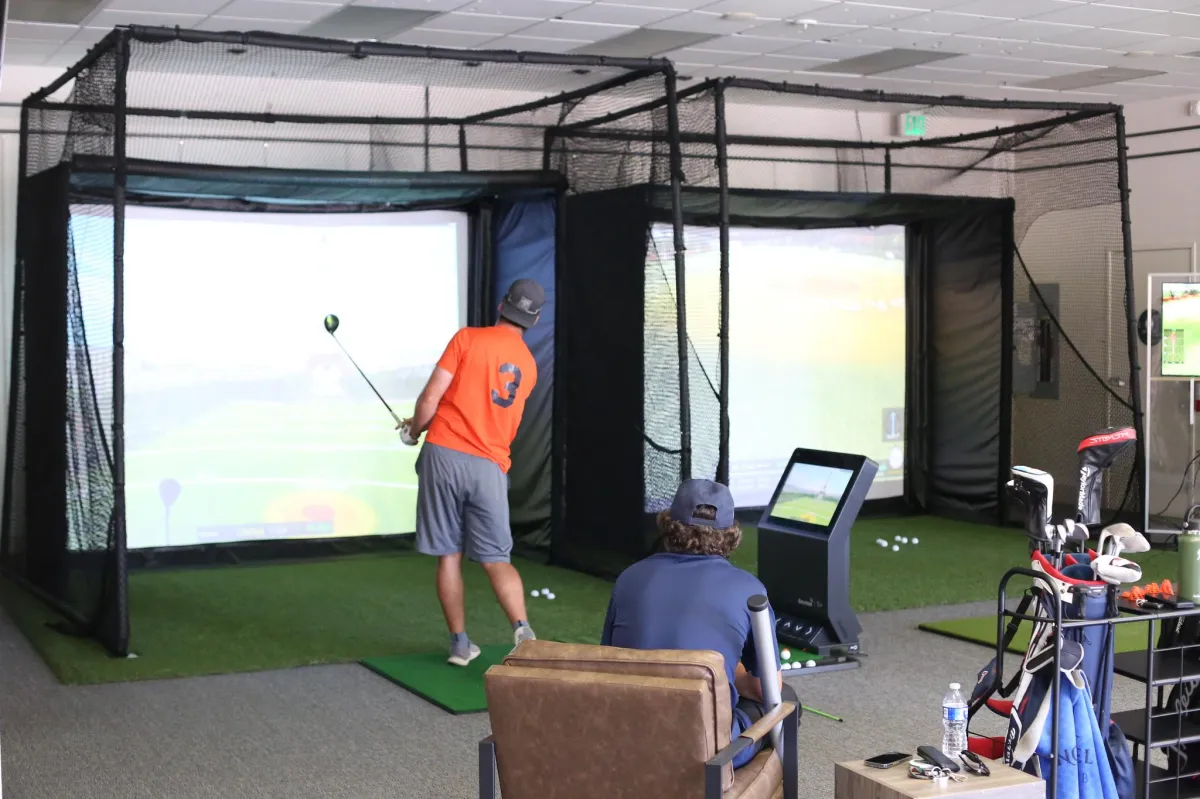 Golf instructor coaching a student in an indoor golf simulator, providing guidance on swing technique and strategy.