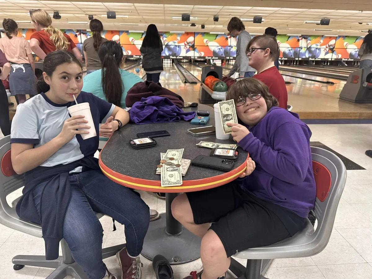 boy and girl at bowling alley smiling and holding up money 