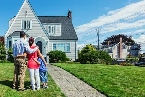 Family of three standing in front of a suburban house with a well-kept lawn, looking at their new home.