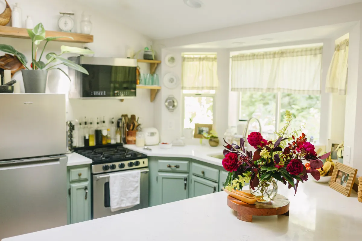Bright kitchen with white marble countertops, a floral arrangement, green cabinets