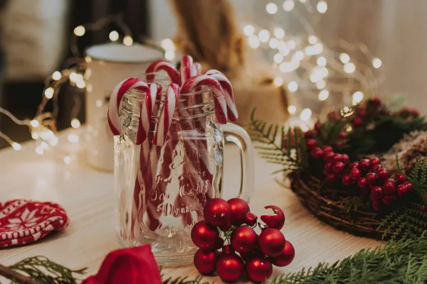 Candy canes in a glass jar surrounded by greenery and holiday lights on a table