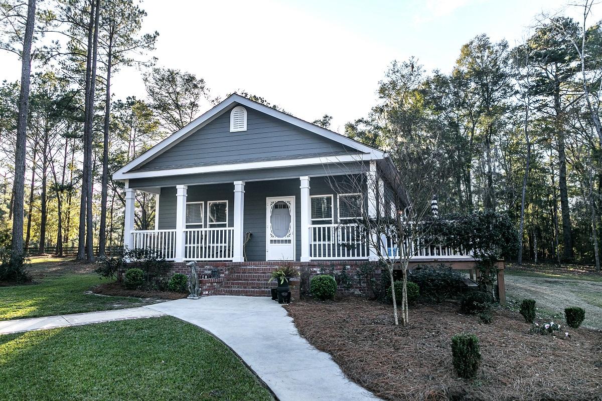 A gray and white mobile home with skirting and landscaping.