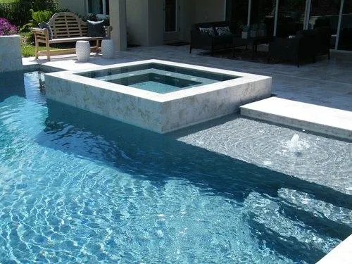 Luxury outdoor pool with raised spa and shallow water fountain next to a modern patio with seating.