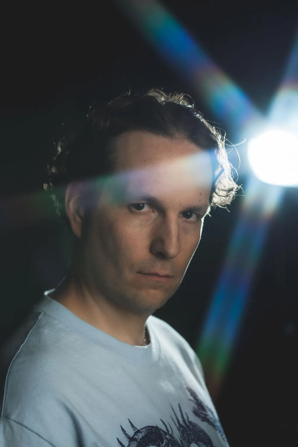 A spotlight shines into the camera flanking graybeat as he turns his head to the side and gazed back at the camera with no sunglasses. beams of light from the bright spotlight behind seem to reach out and run across his forehead