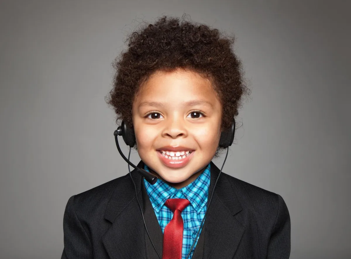 Smiling young boy in a suit and tie wearing a headset, posing confidently against a gray background