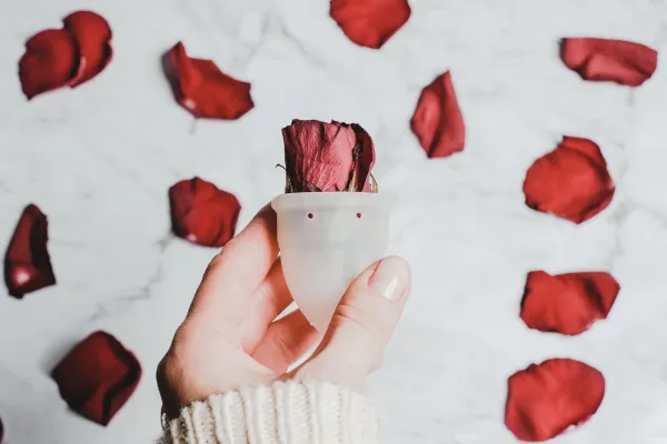 A hand holding a menstrual cup with a cascade of red rose petals