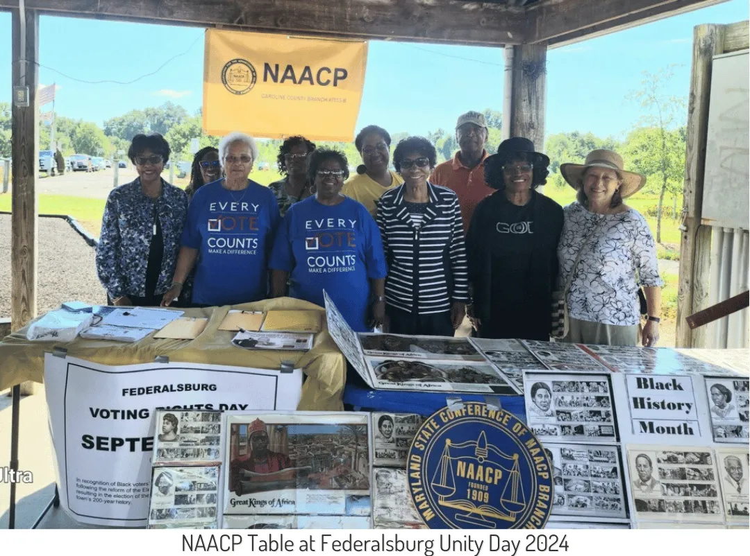 A group of people stand and smile behind the NAACP table at Federalsburg Unity Day 2024.