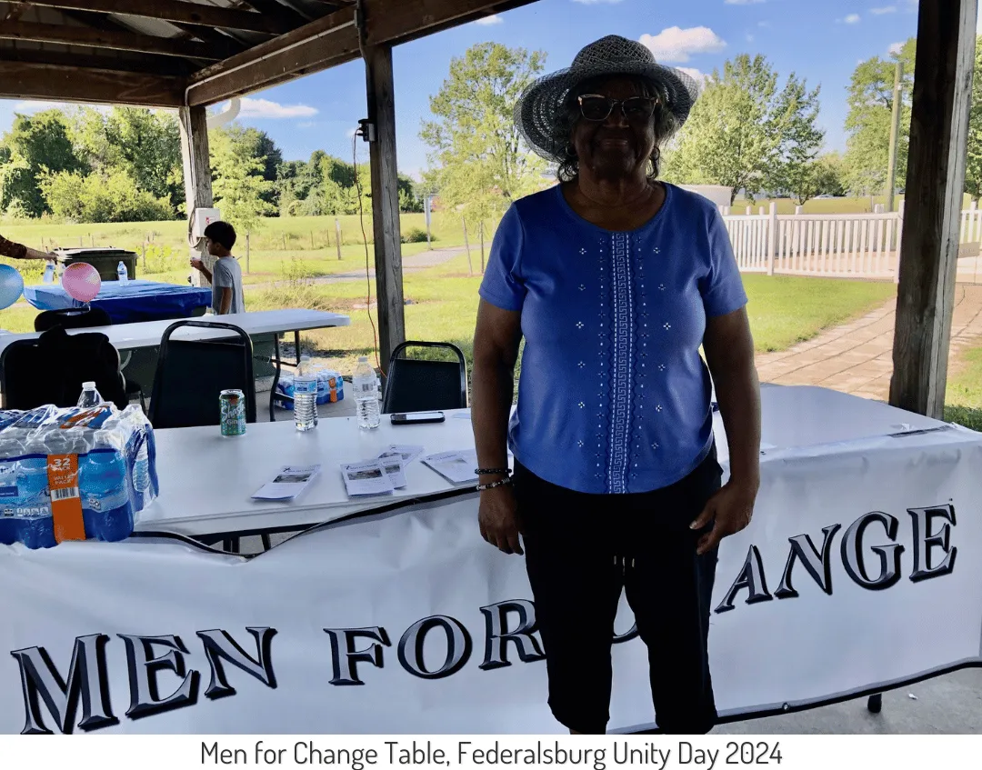 A woman stands in front of a table labeled "MEN FOR CHANGE" at Federalsburg Unity Day 2024.