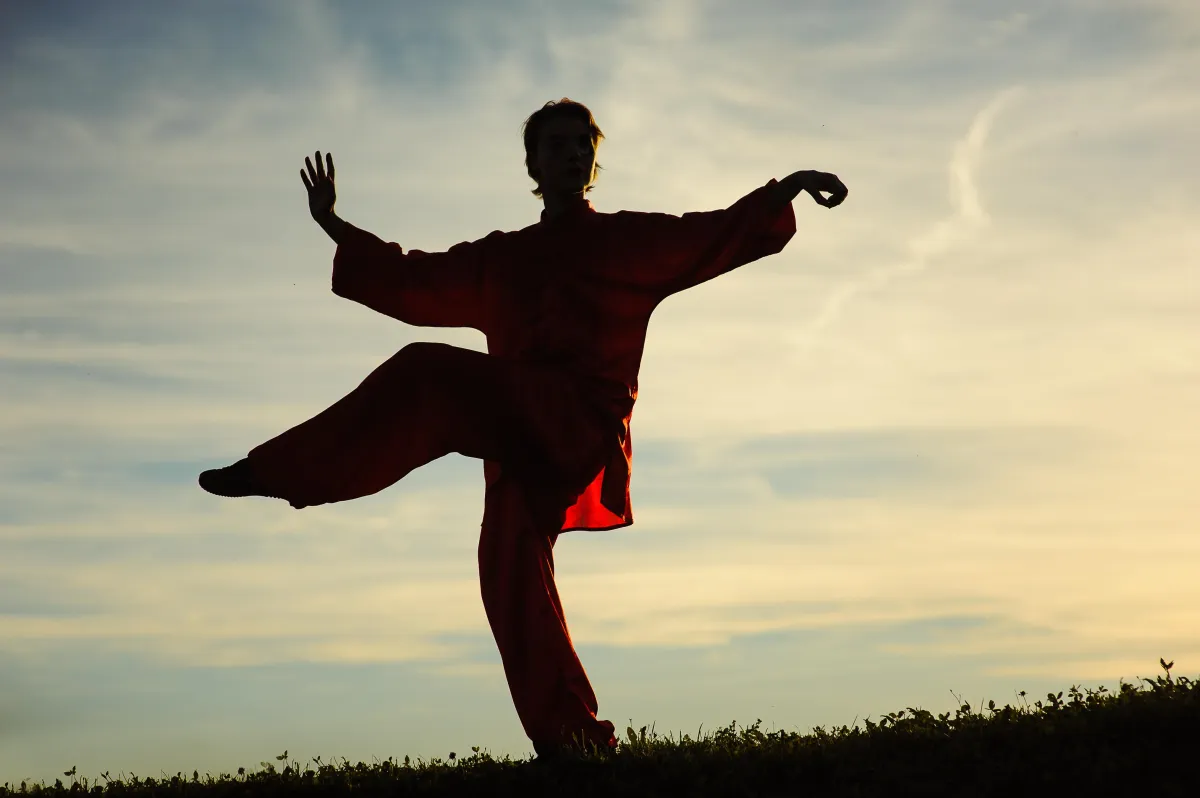 Woman doing tai chi on mountain edge with leg raised