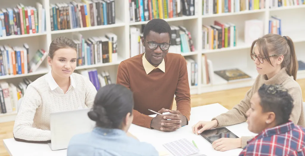 Diverse group of professionals in discussion around a table in a library setting.