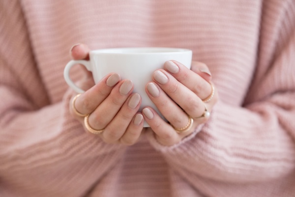 Hands wrapped around a warm mug, wearing a soft sweater, conveying comfort, regulation, and quiet reflection.