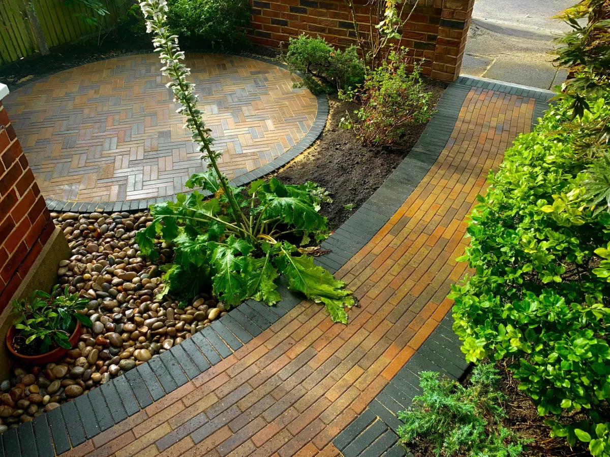 An inviting and beautifully designed block paved patio in Twickenham, surrounded by lush greenery. A well-crafted pathway leads to the house, with a captivating circular feature adding elegance to the landscape 