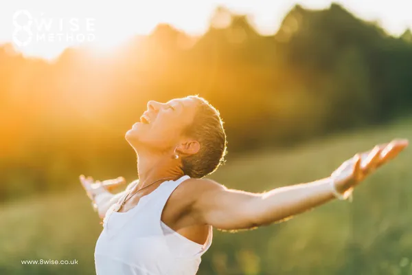 Woman in a field a sunrise with arms outstretched smiling at the sky 