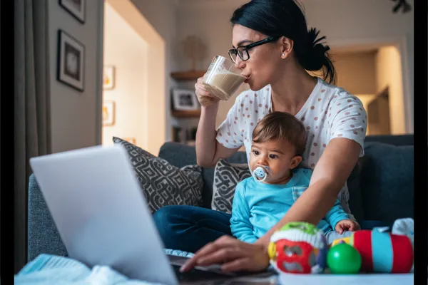 Mom holding a baby while working on laptop