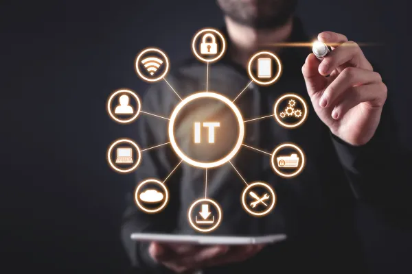 A business professional in a dark outfit using a stylus to interact with a futuristic digital interface displaying interconnected IT-related icons, including cloud computing, cybersecurity, networking, and system management. The glowing technology hub in the center highlights the concept of IT strategy and digital transformation.