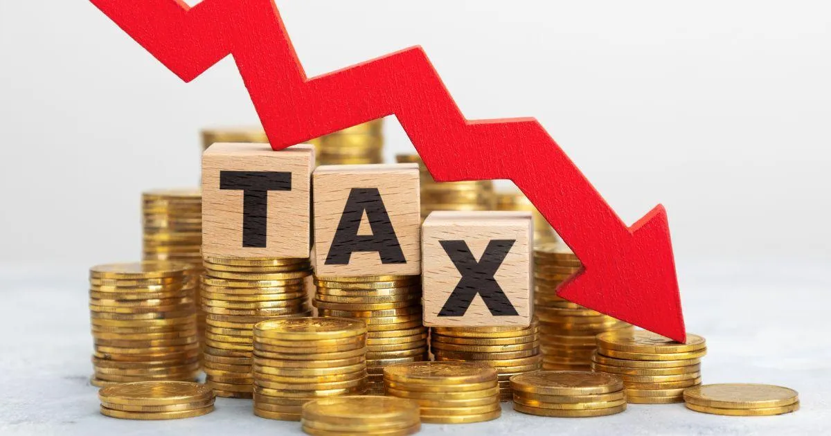 Red downward arrow over stacks of coins with wooden blocks spelling TAX, representing tax cuts and reduced tax burden.