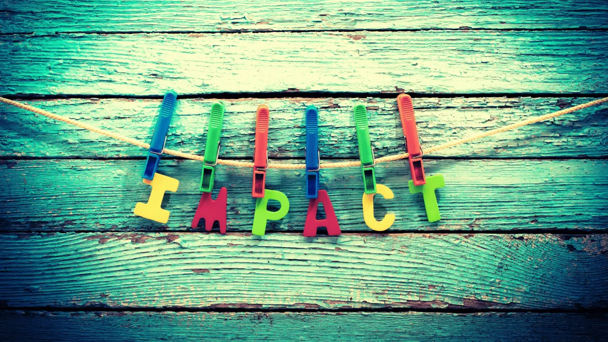 Green wood background with the word IMPACT hanging by clothes pins on a peice of twine in primary colors.