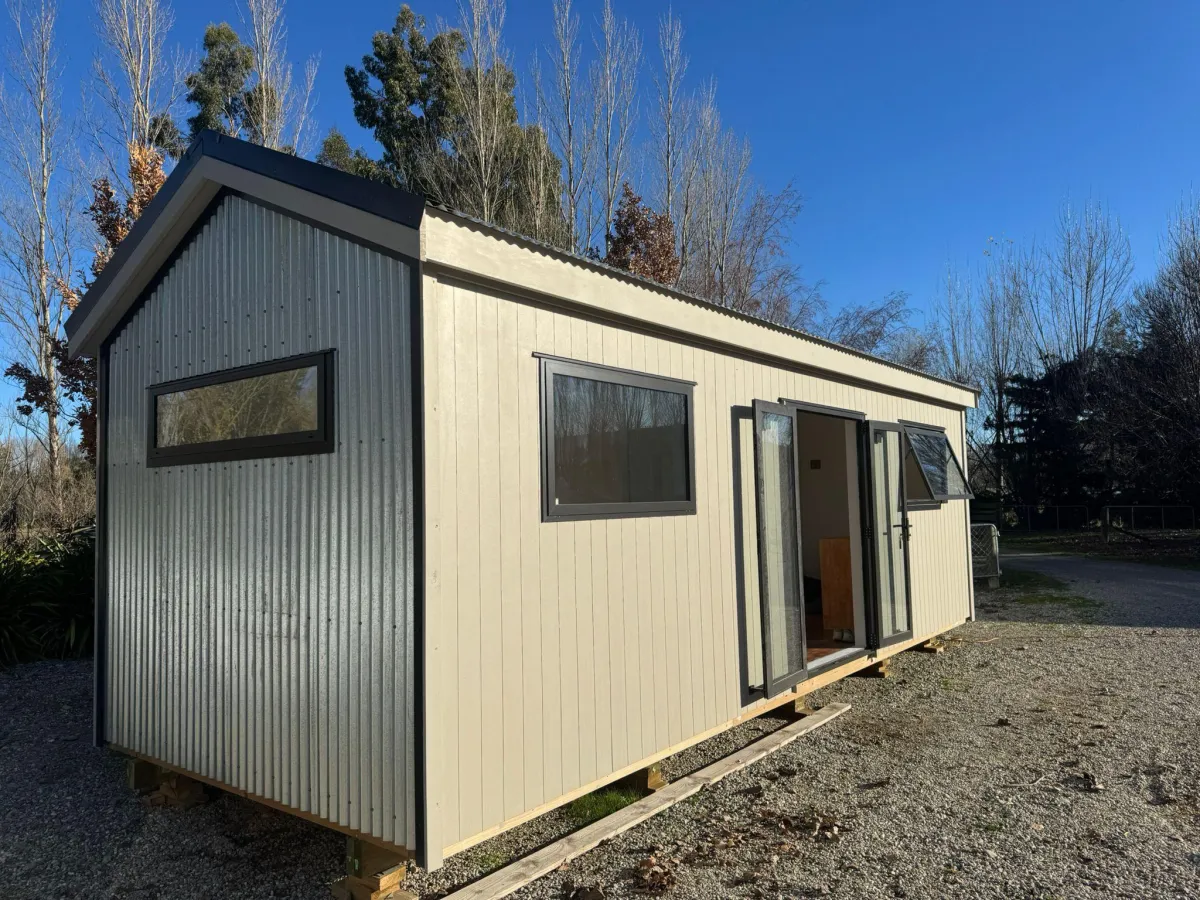 Exterior of modern beige cabin with black window frames and double doors in Alexandra, Central Otago.