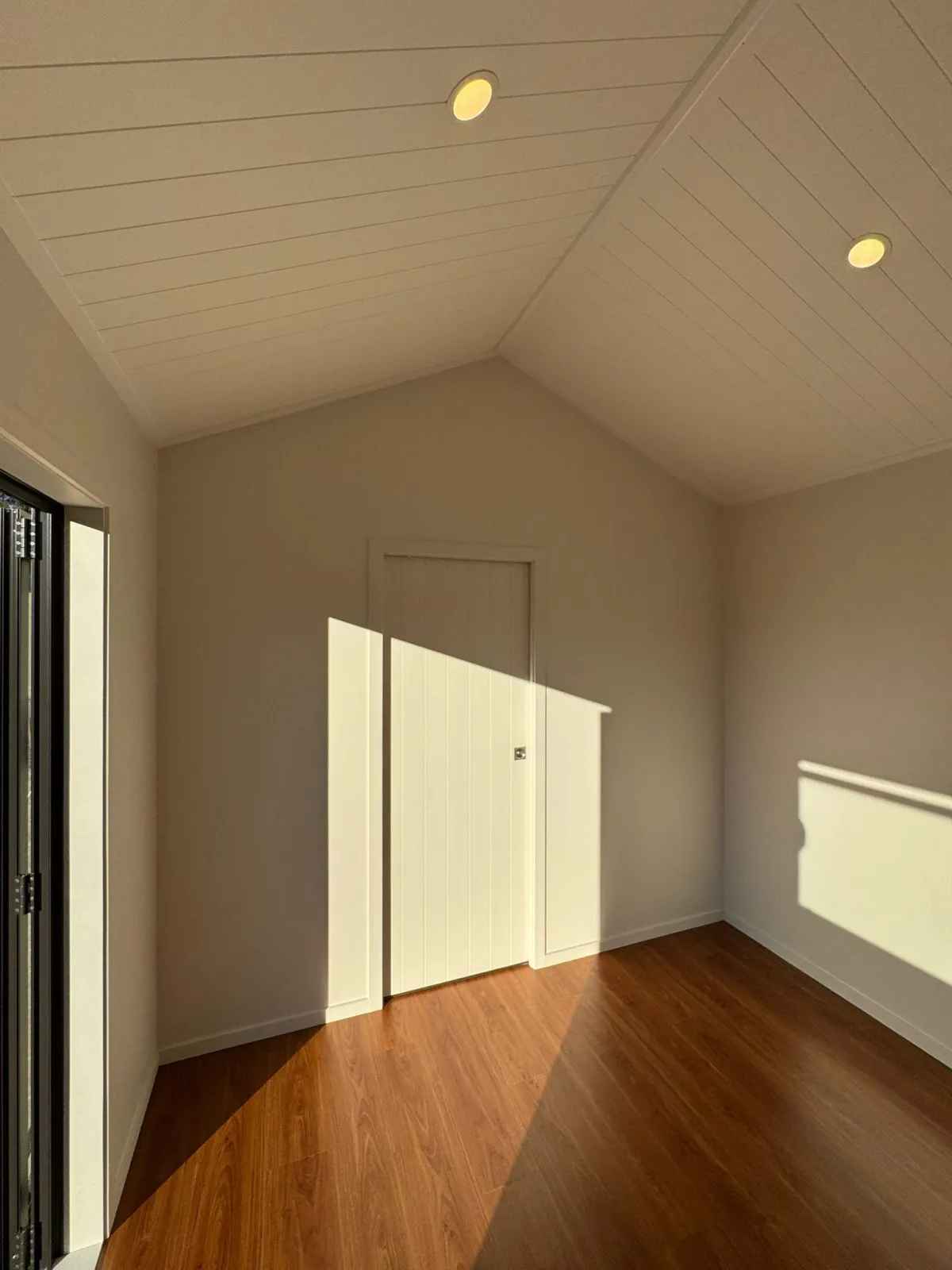 Carpeted sleepout room in portable cabin with grooved interior door and double-glazed windows.