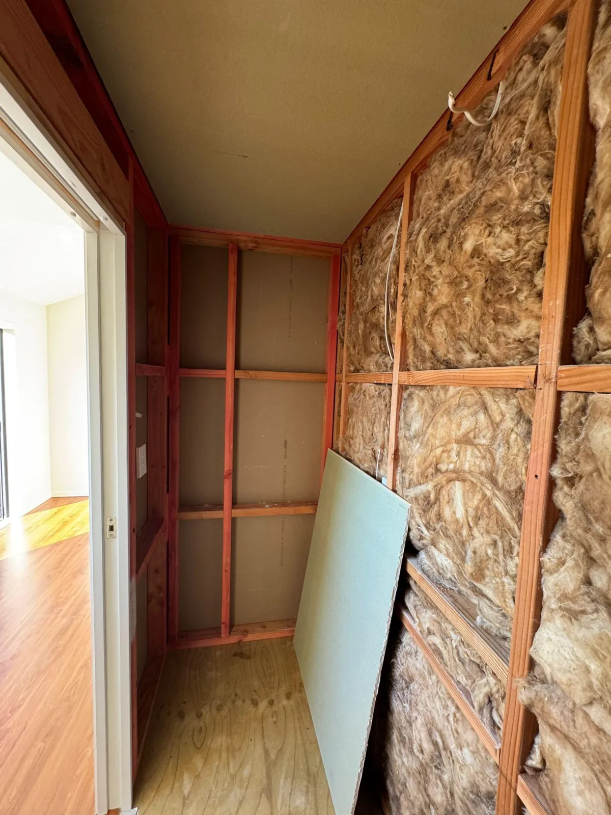 Different view of insulated unfinished room inside cabin with timber framing and wall insulation.