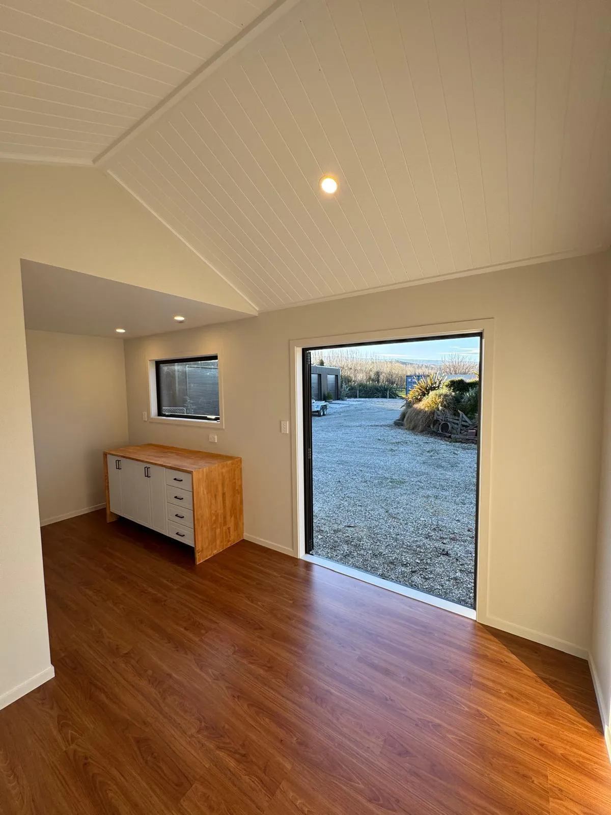Interior of tiny home with wood-look floors, white ceiling, and open doors letting in natural light.