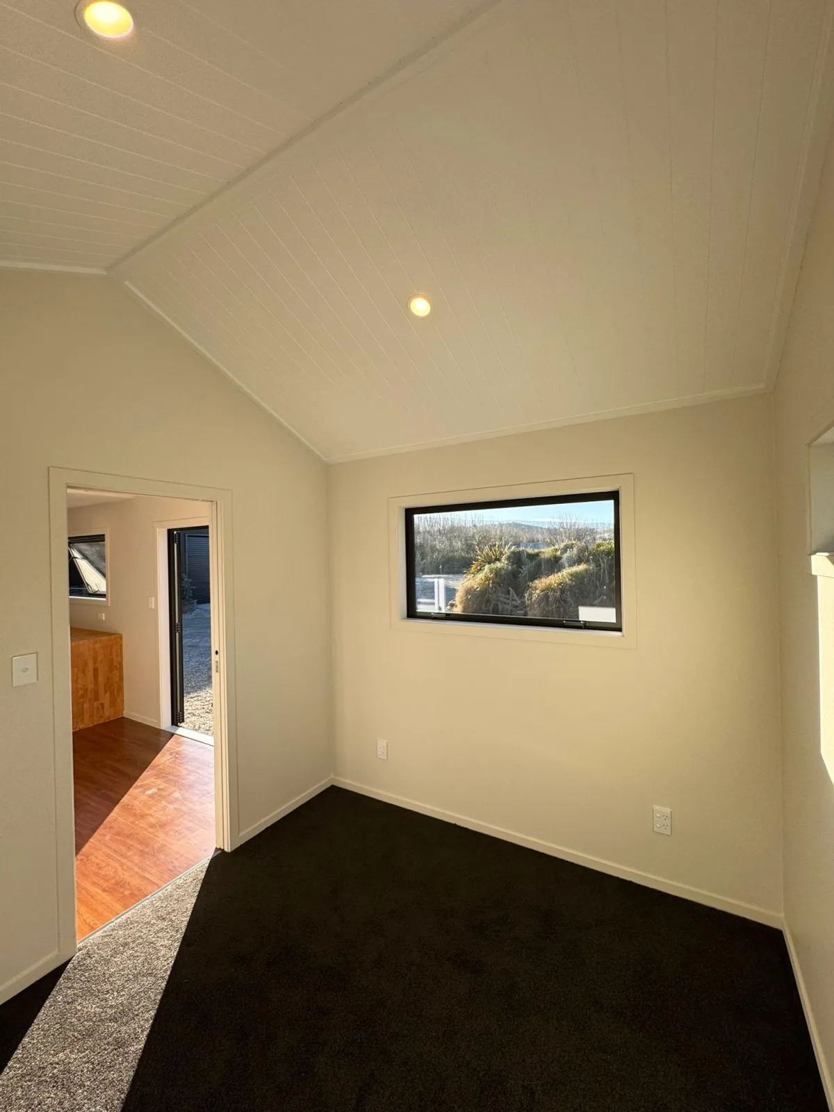 Carpeted room with gable ceiling and window in sleepout cabin in Alexandra.