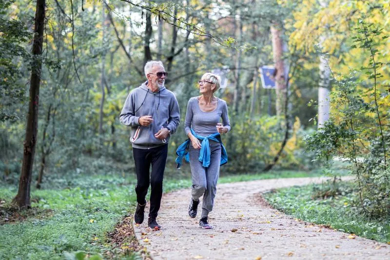 older man and woman jogging through park