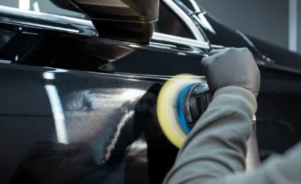 Professional using rotary polisher on black car panel.