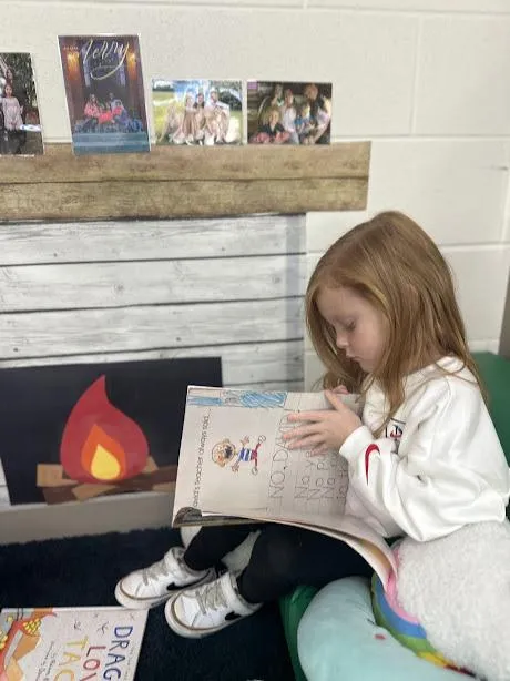 Little girl reads No David by a paper fireplace.