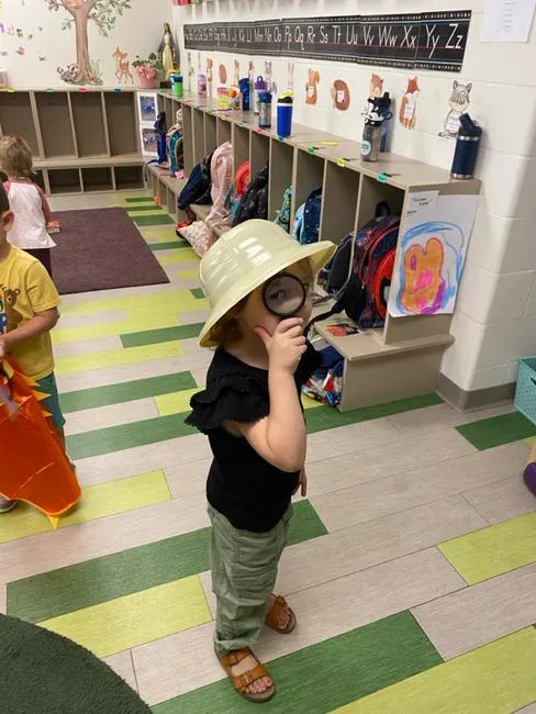 Small child dressed as an explorer looks through a magnify glass