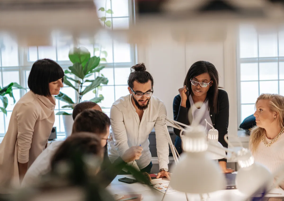 Small group of people, some standing, some sitting around an office desk, in discussion